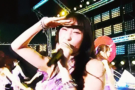 dambara ruru performing at summer fes 2025 with juice=juice. the camera is pointed close to her face; she's doing a 'looking for someone' pose with her arm, then lowers it to point at the camera and smile brightly before turning away. the gif is very vibrant with visual noise added on top